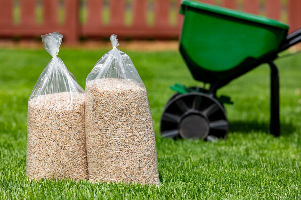 bags of fertilizer sitting on a green lawn with a fence in the background