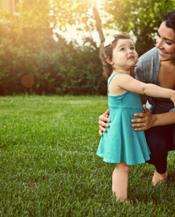 Mother and toddler hugging on a green lawn in the backyard