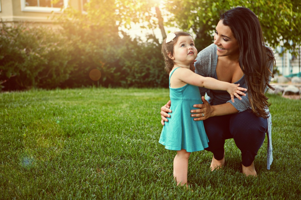 Mother and toddler hugging on a green lawn in the backyard